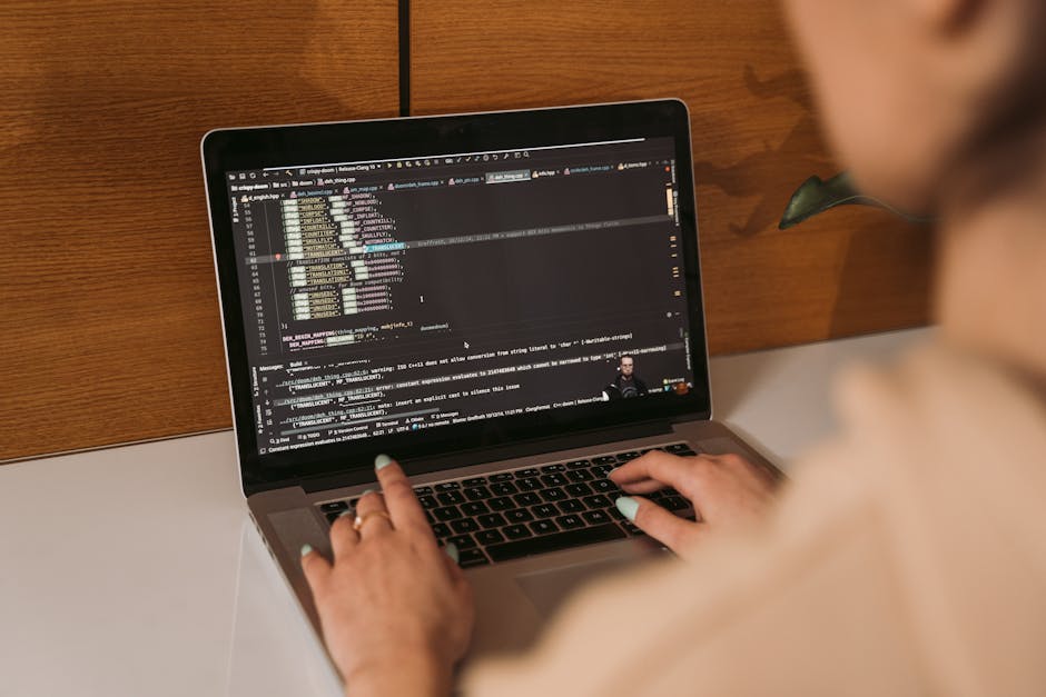 Close-up view of a laptop computer displaying lines of computer code on its screen. The code is highlighted in various colors, indicating programming language syntax, set against a dark background. Th